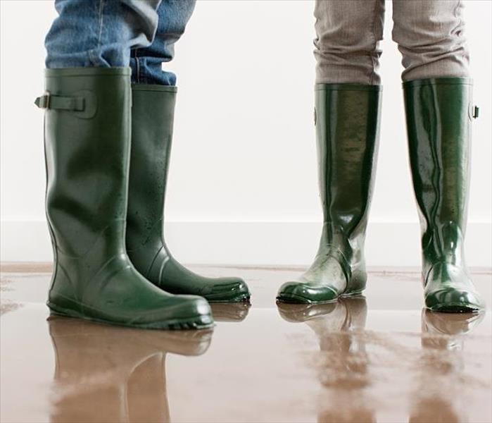 Two people standing with green boots on. 